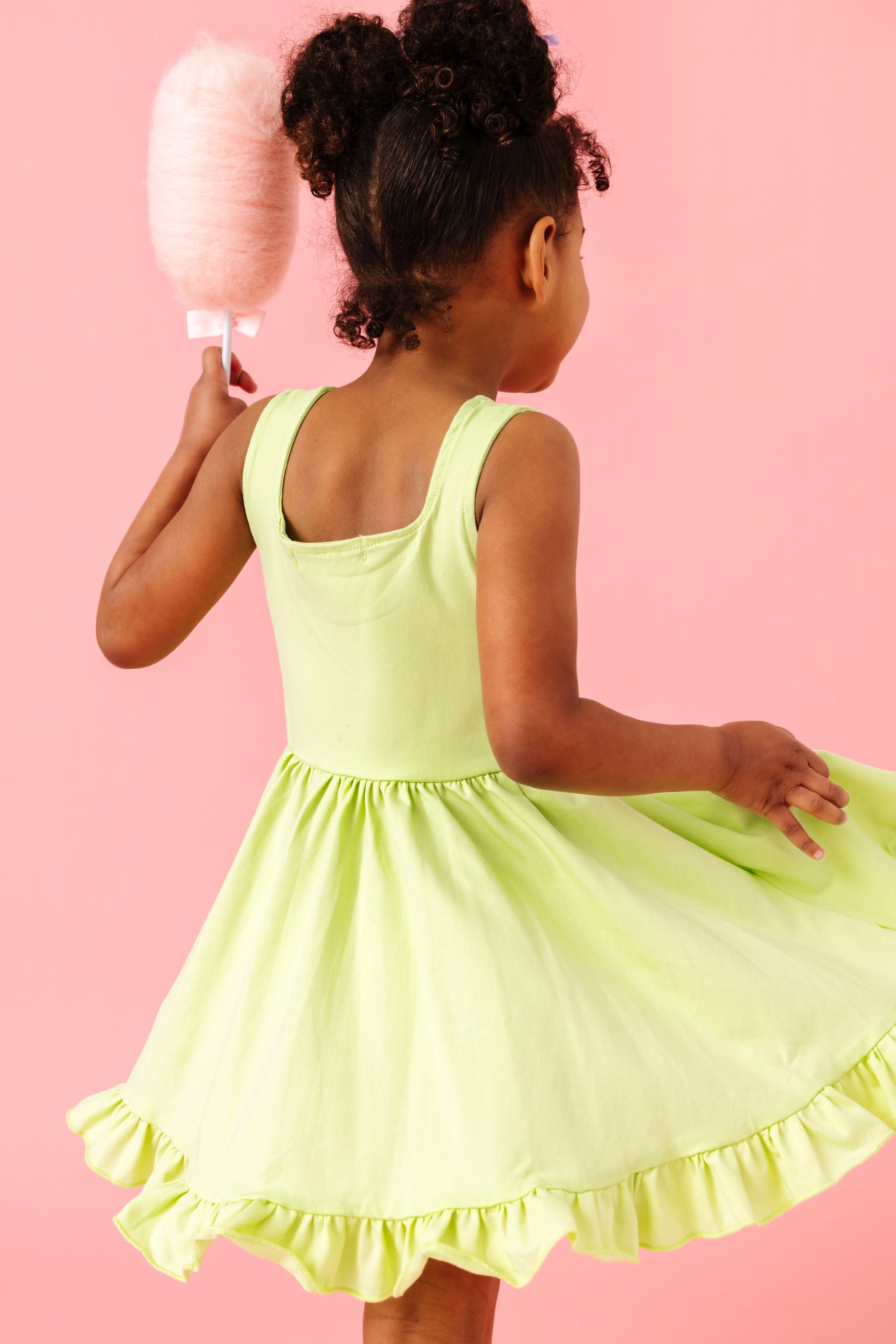 back view of little girl twirling with cotton candy in lime green square neck sleeveless summer twirl dress