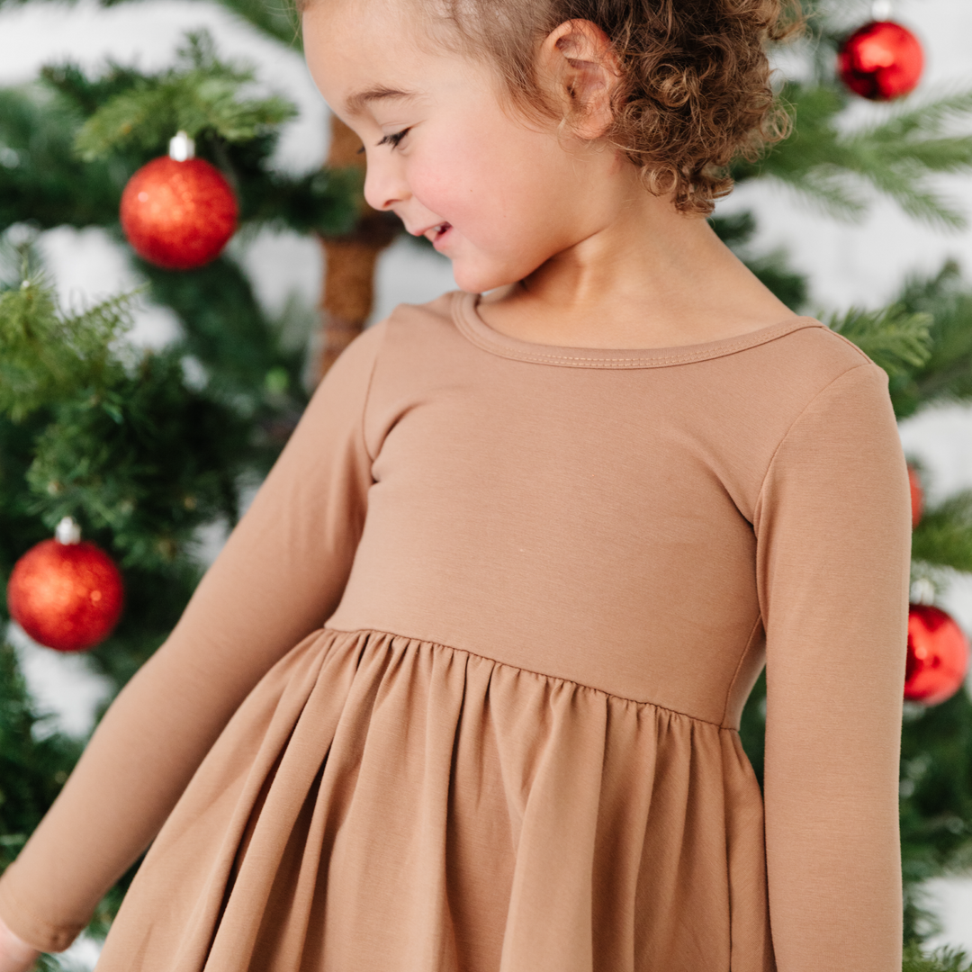 girl in mocha brown long sleeve twirl dress in front of christmas tree