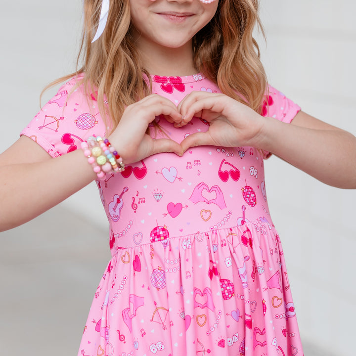 swiftie girl with heart hands and friendship bracelets wearing taylor inspired valentine's dress