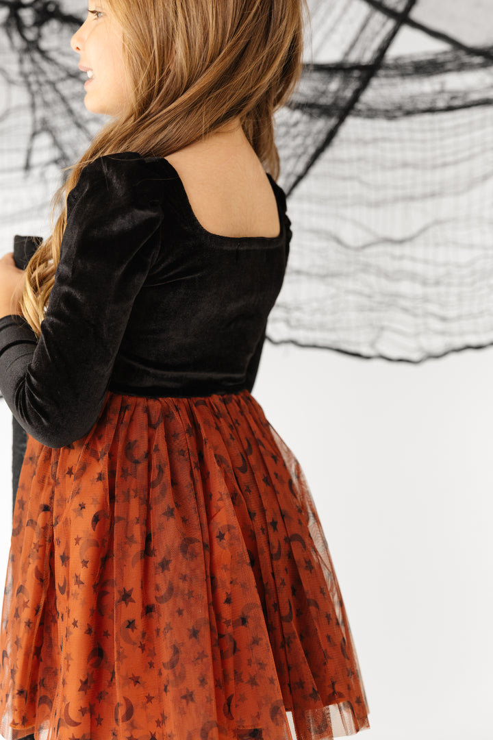 back view of little girl in square neck long sleeve dress with black velvet bodice and rust tulle skirt with moon and star print 