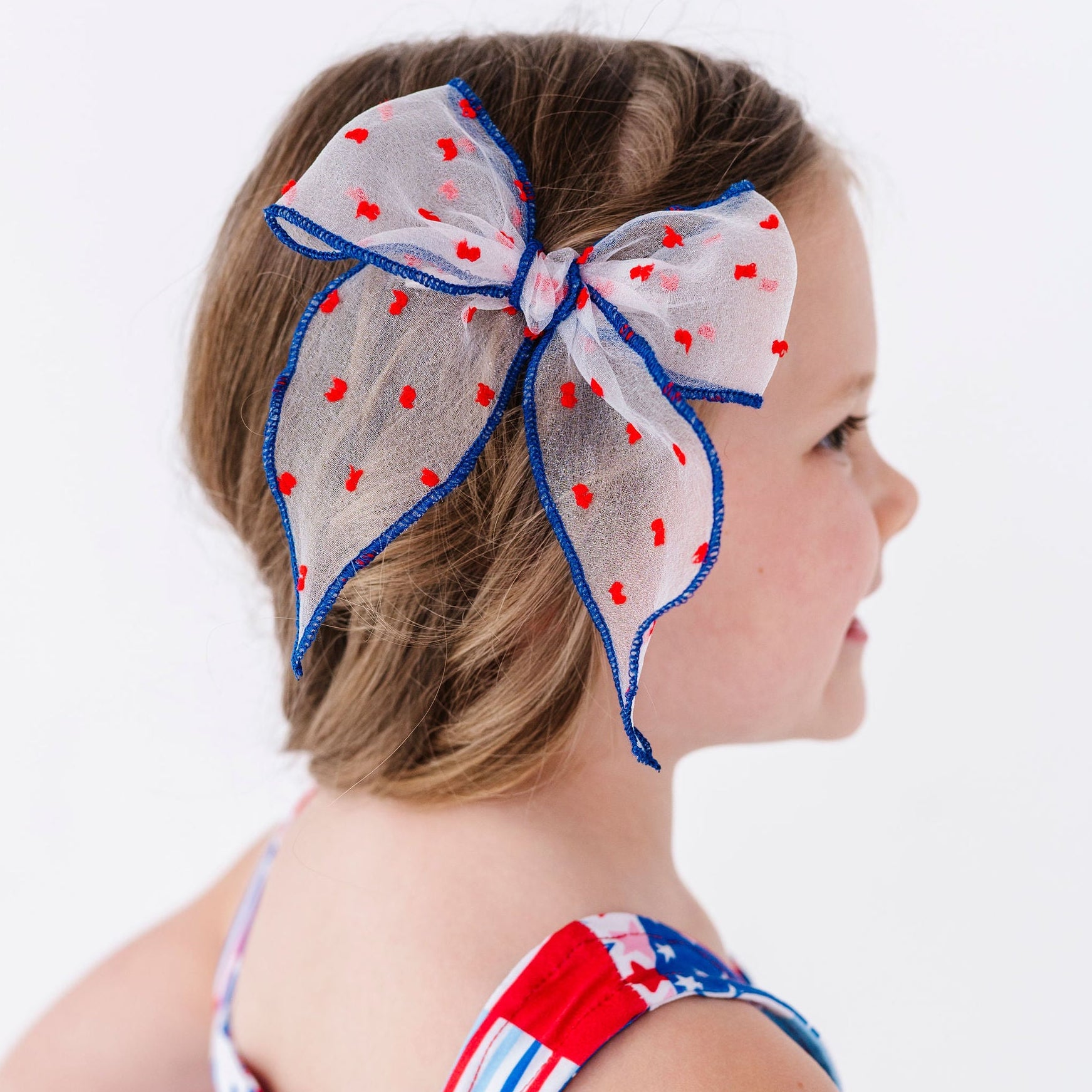 young girl wearing sheer white hairbow with blue trim and red dots for the 4th of July
