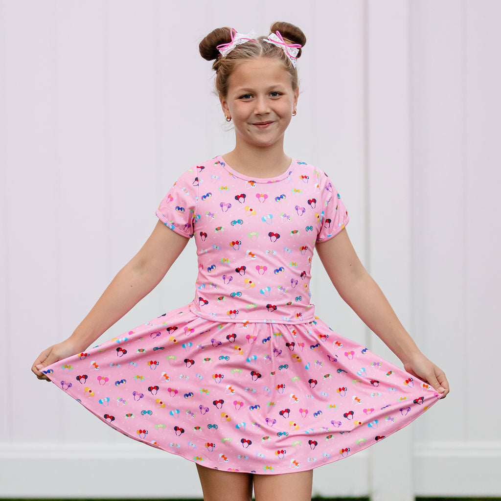 Young girl wearing a pink dress with bow patterns against a white background