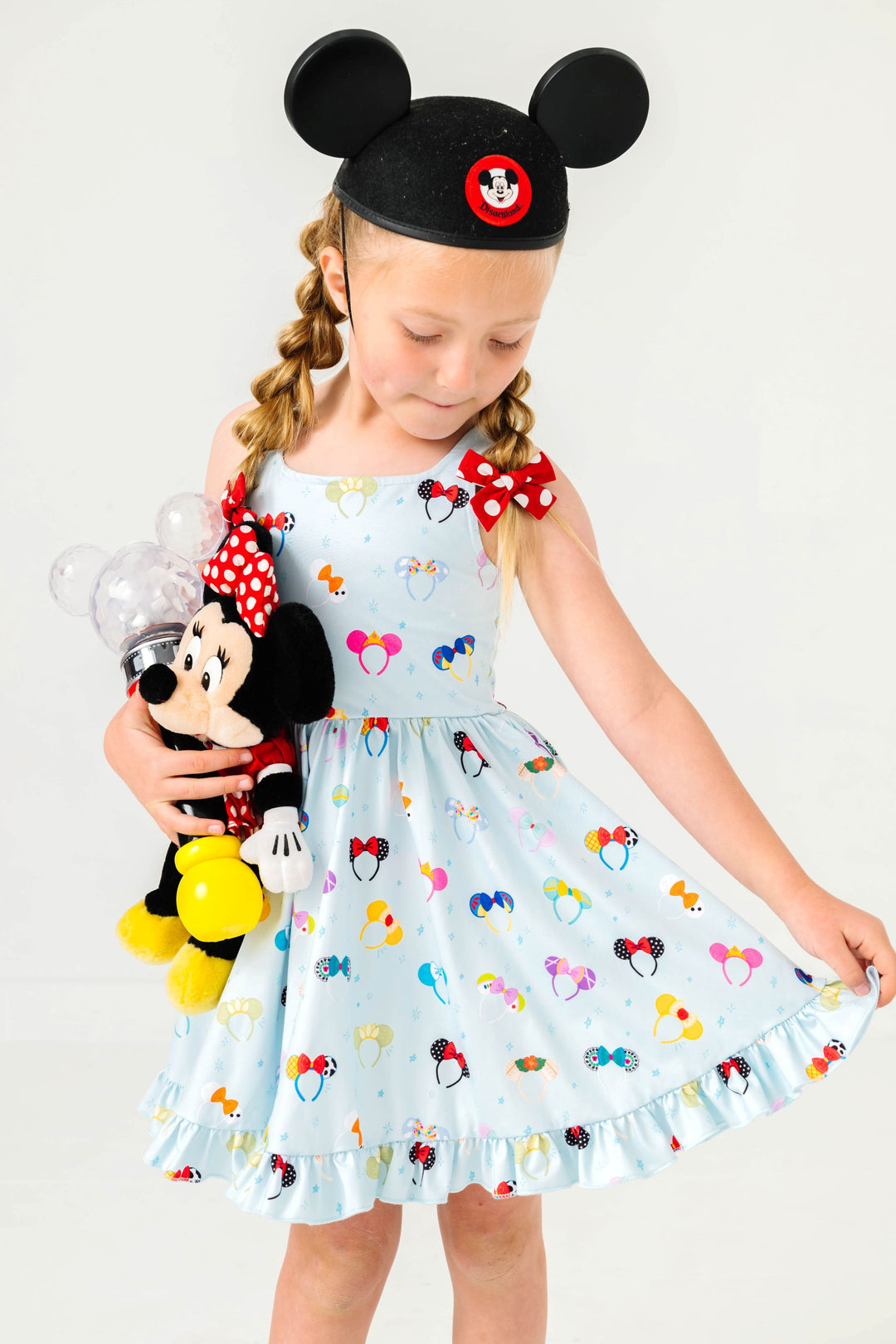 little girl in blue magical ears sleeveless twirl dress styled with minnie dot pigtail bows, ears and minnie stuffed toy 