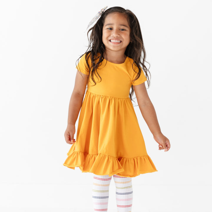 little girl in school bus yellow twirl dress and rainbow striped tights