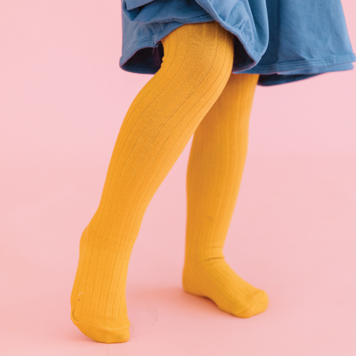 girl in marigold yellow ribbed tights and blue dress on pink background