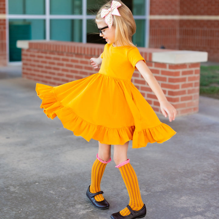 little girl twirling in marigold yellow cotton twirl dress with matching back to school pencil socks