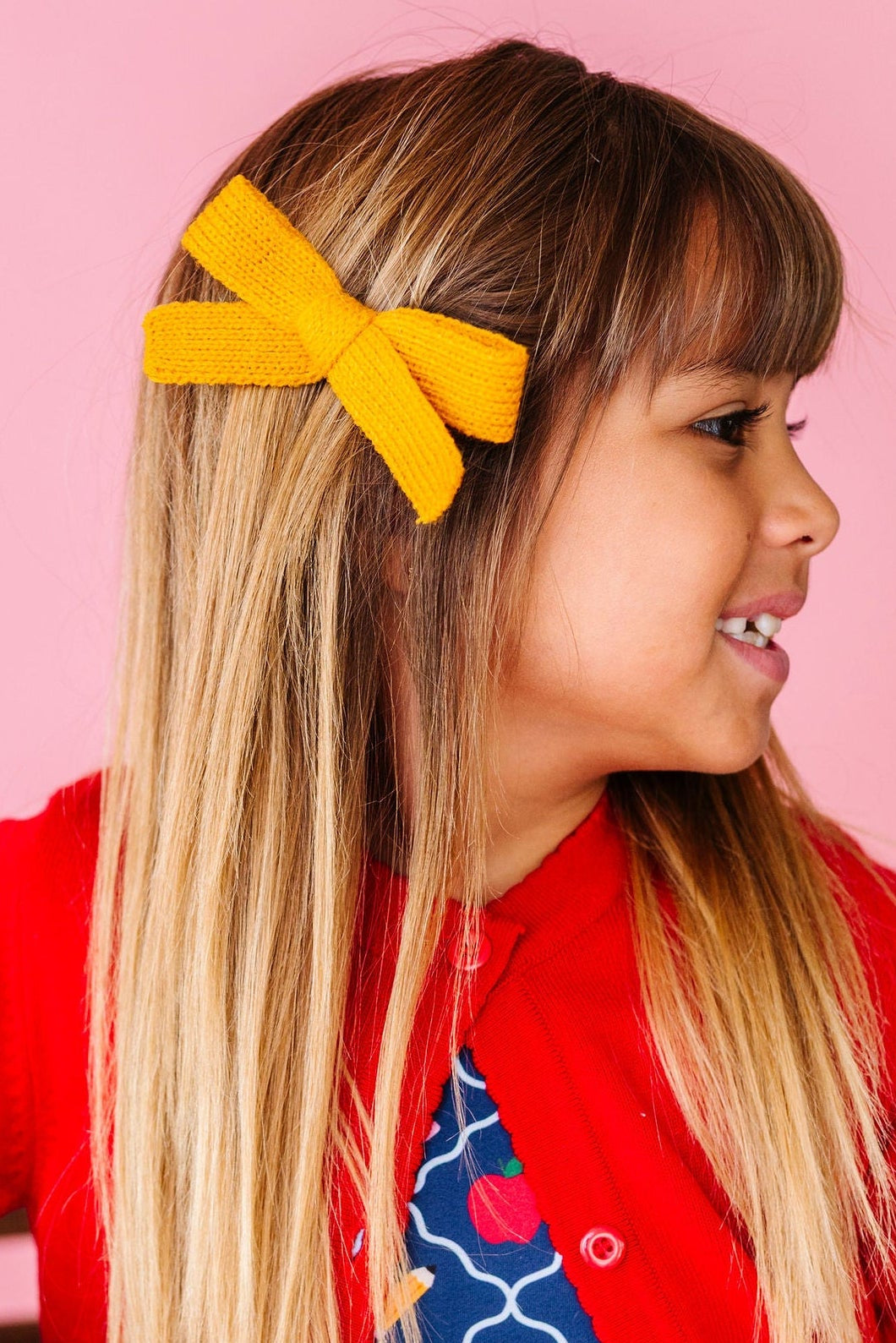 girl wearing yellow yarn knit hair bow with back to school dress and red cardigan