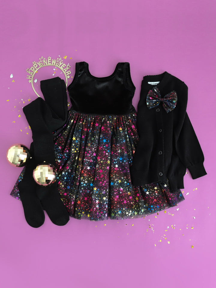 flatlay of girls new years eve outfit with sleeveless metallic stars tutu dress and black cardigan and black fancy knit tights with matching metallic starts tutu bow