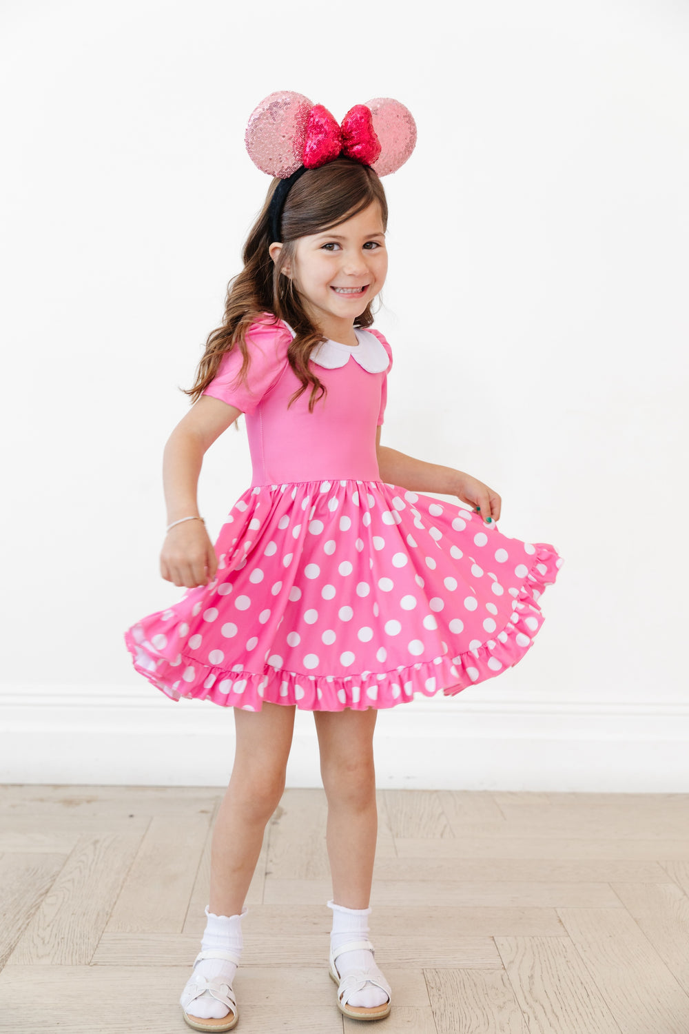 girl in pink minnie mouse character twirl dress that is pink with white collar and pink polkadots on skirt wearing mouse ears