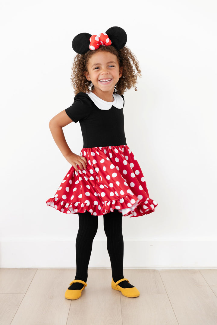 little girl with Minnie Mouse headband wearing classic red polka dot Minnie inspired twirl dress paired with black ribbed tights and yellow mary janes