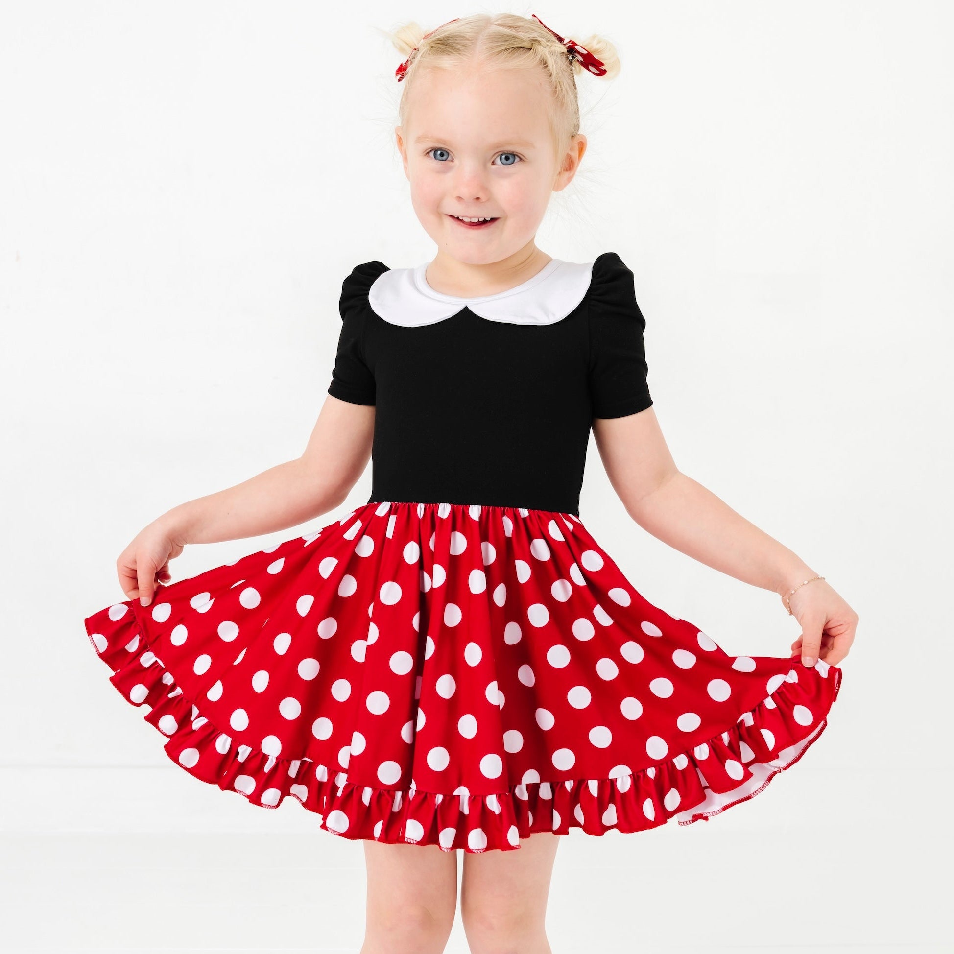 Child wearing a black top with white collar and red polka dot skirt on a white background
