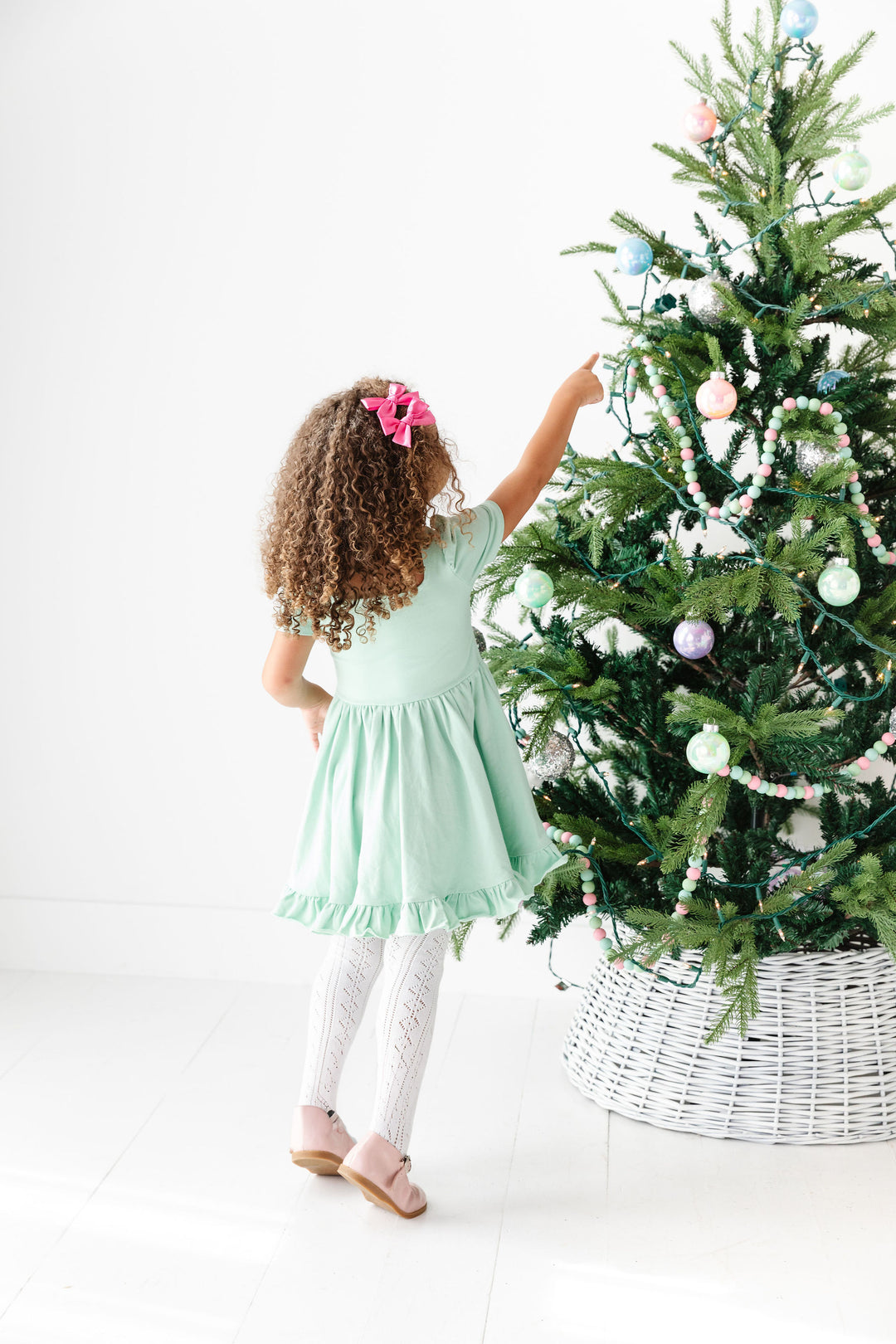 little girl in front of christmas tree wearing mint green twirl dress and pink hair bows