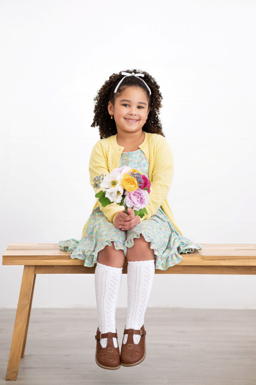 little girl sitting with spring flower bouquet in mint green floral twirl dress paired with pastel yellow pointelle cardigan and white open knit knee socks