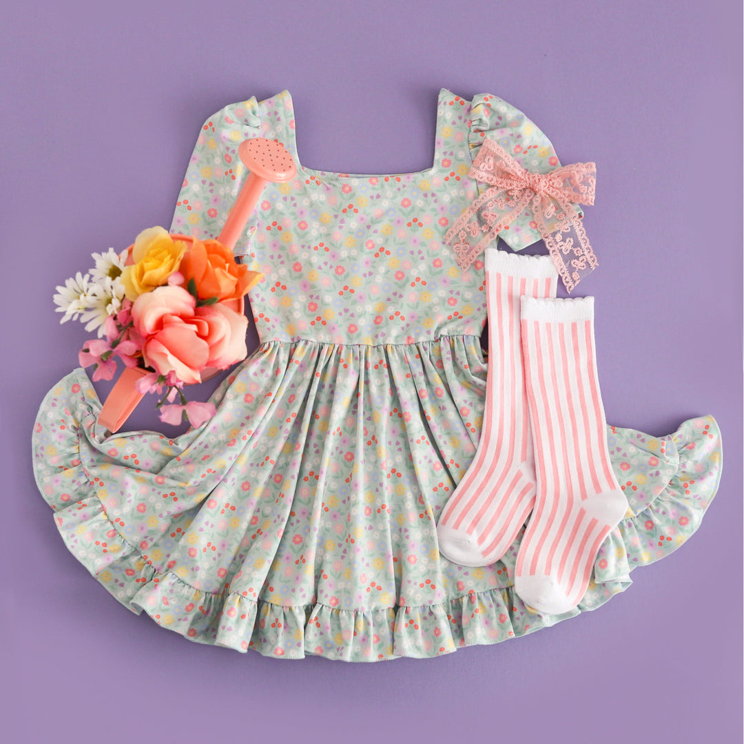 spring flat lay for girls' soft mint twirl dress with petite pastel spring floral print styled with white and light pink vertical striped knee socks, pink lace hair bow and watering can filled with flowers