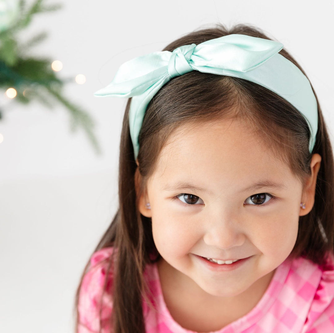 little girl in mint colored satin headband with top knot wearing pink dress