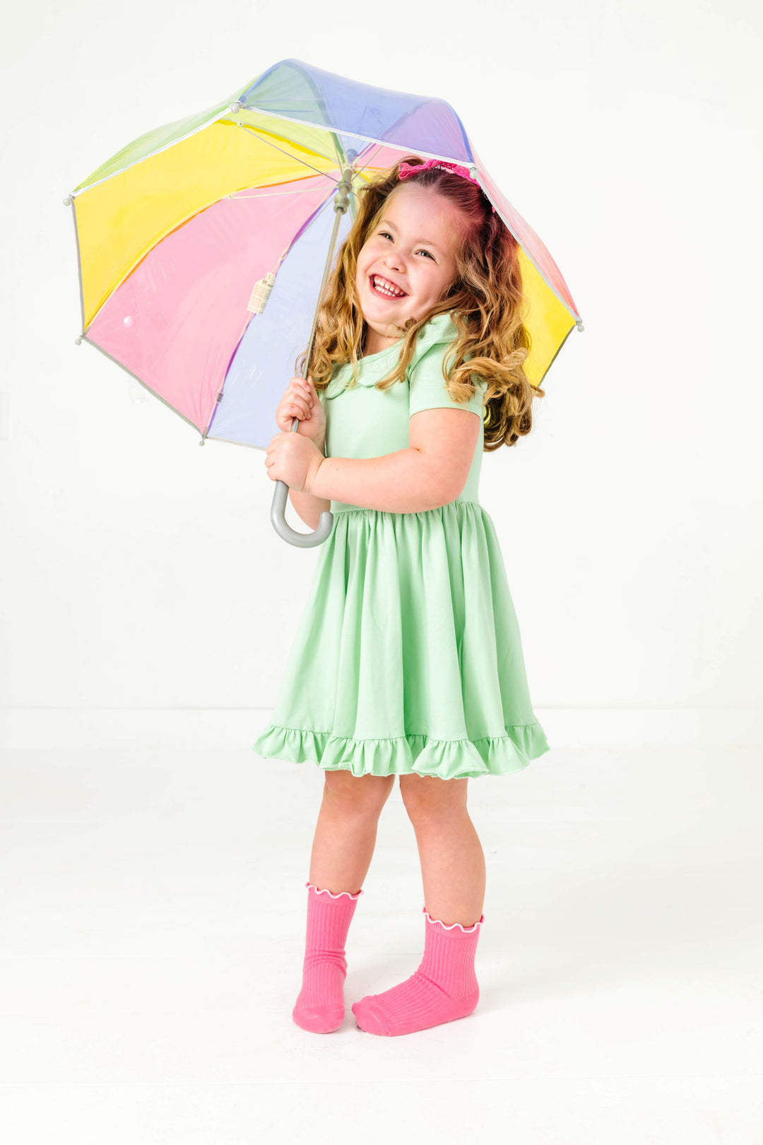 young girl holding pastel rainbow umbrella in mint green cotton blend twirl dress paired with pink socks and bows