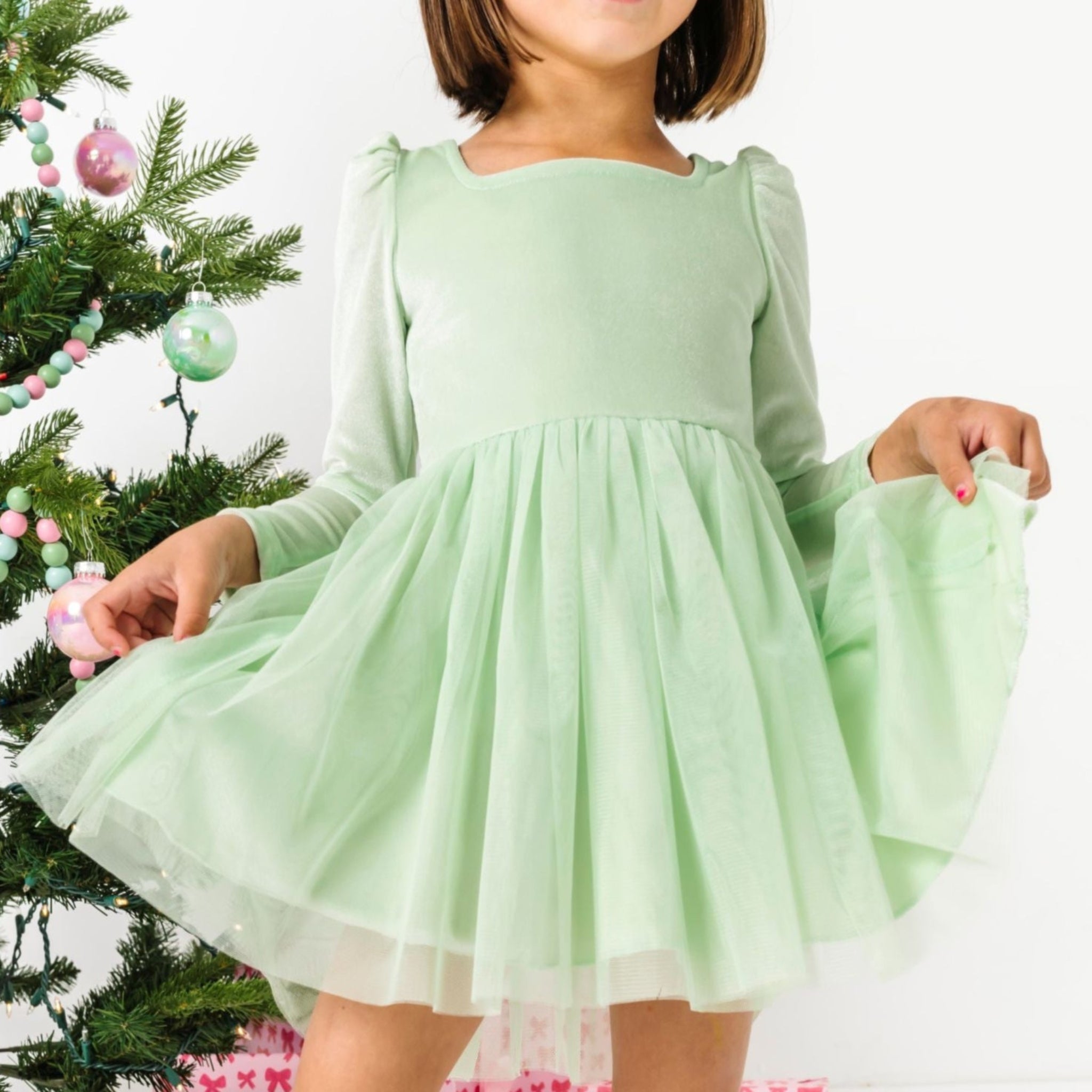 young girl standing by Christmas tree with pastel ornaments in mint green velvet tutu dress with long sleeves