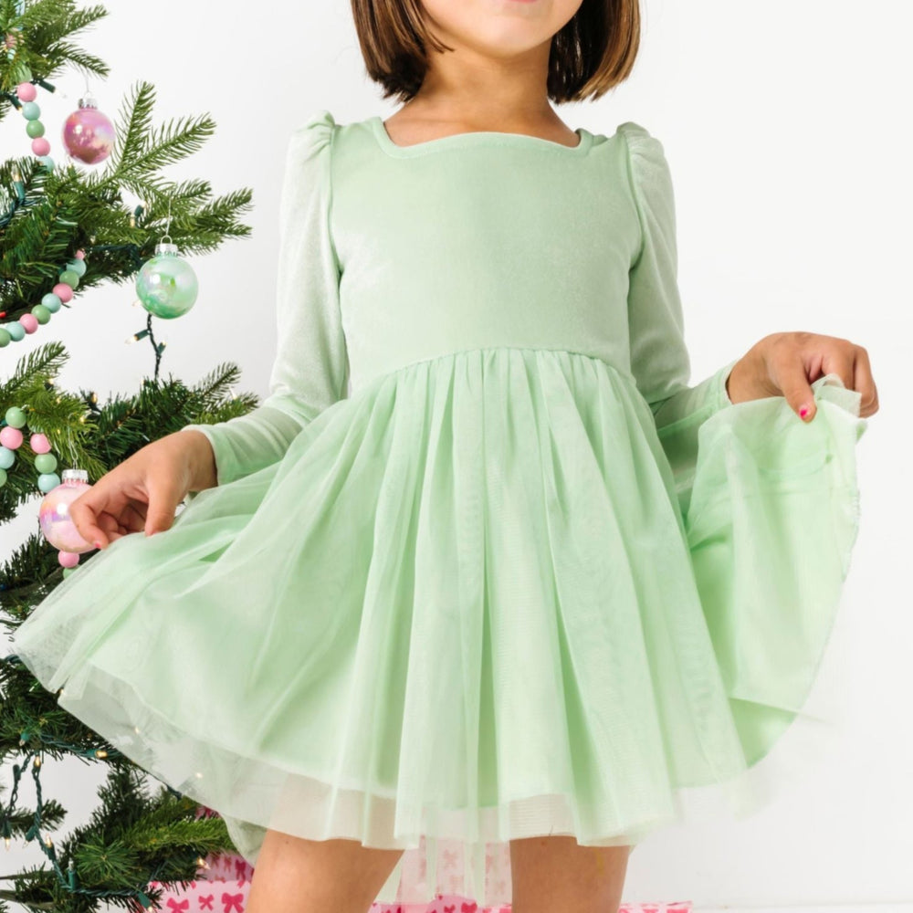 young girl standing by Christmas tree with pastel ornaments in mint green velvet tutu dress with long sleeves