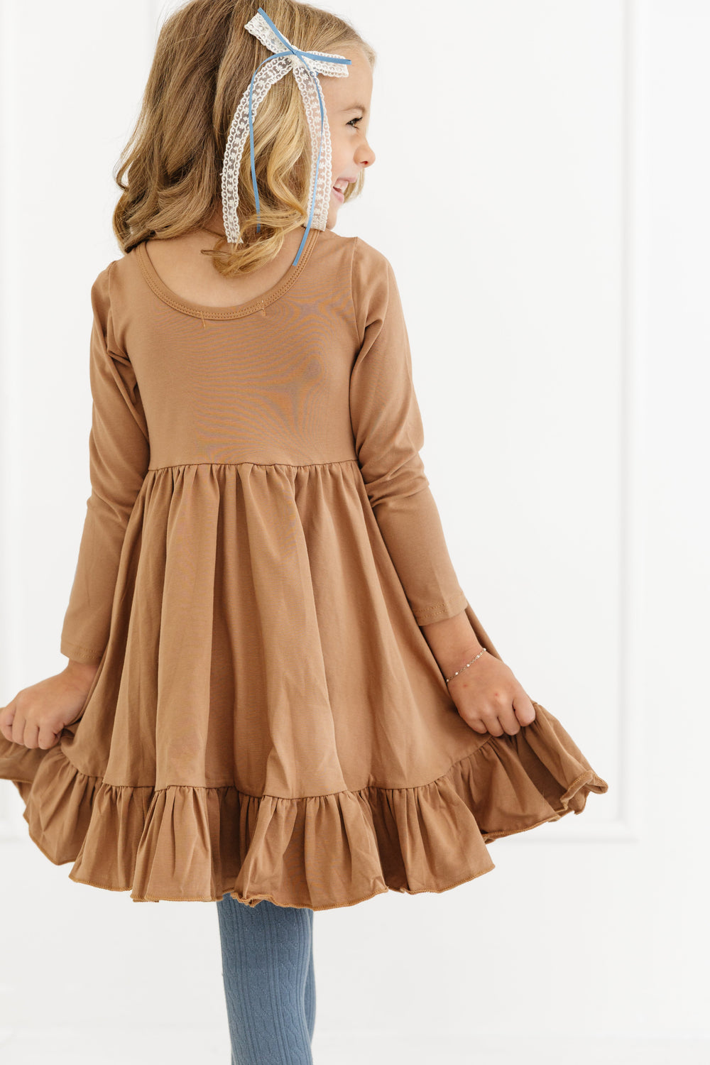 little girl in light brown cotton blend fall twirl dress with long sleeves and ruffle hem paired with denim blue cable knit tights and matching lace hair bow