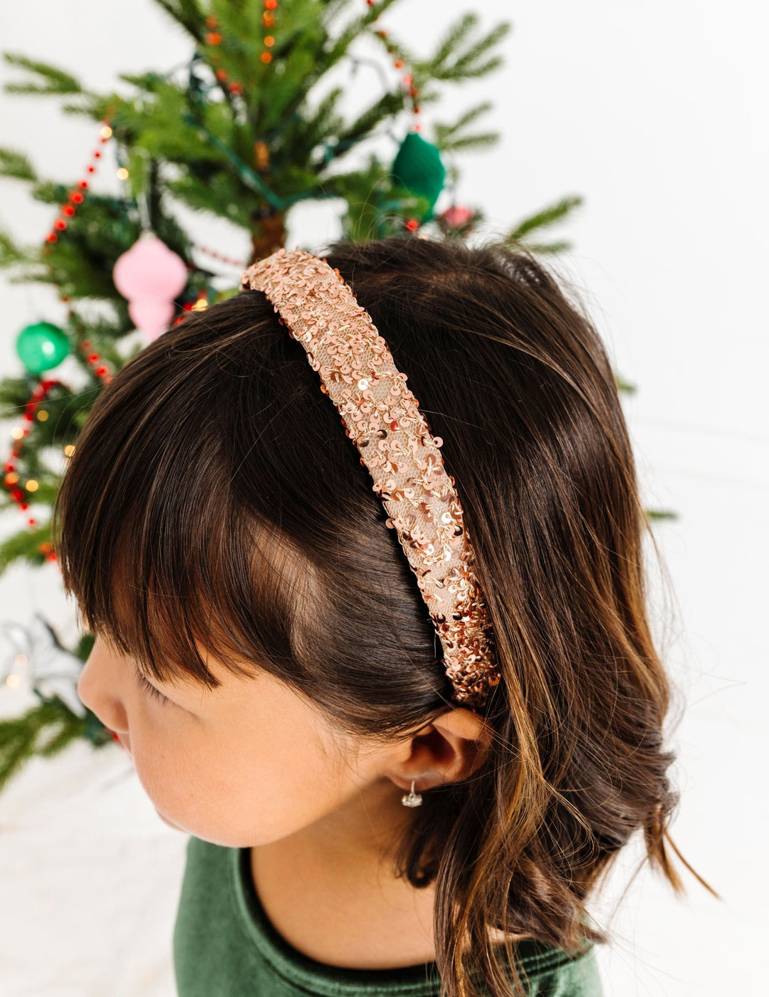 little girl in front of Christmas tree with champagne colored sequin headband paired with forest green velvet dress