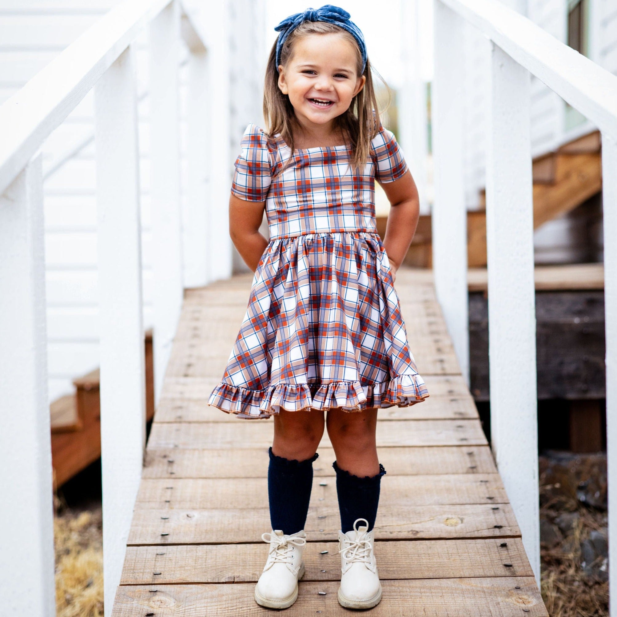 little girl with hands behind back wearing ivory and fall toned plaid twirl dress