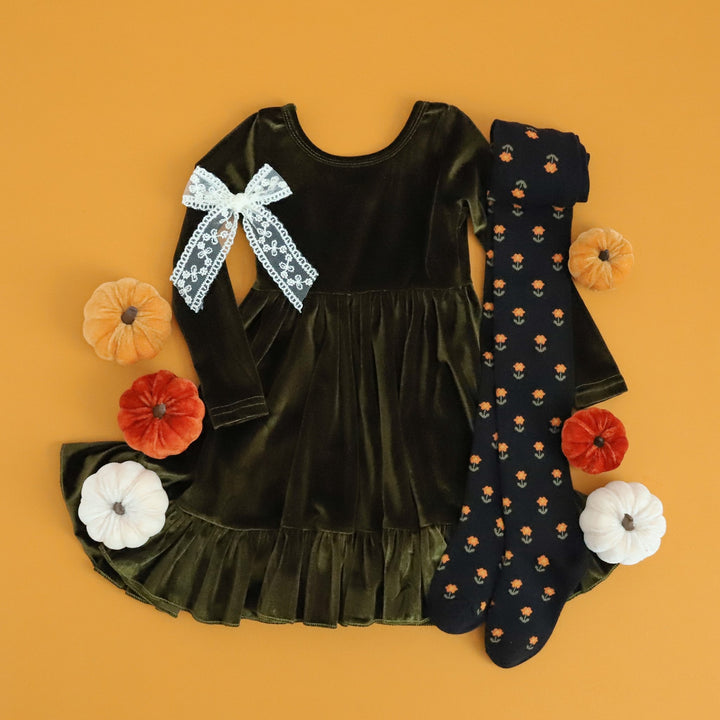 styled flatlay of girls green velvet Thanksgiving dress with coordinating black knit tights with little yellow flowers and ivory lace bow