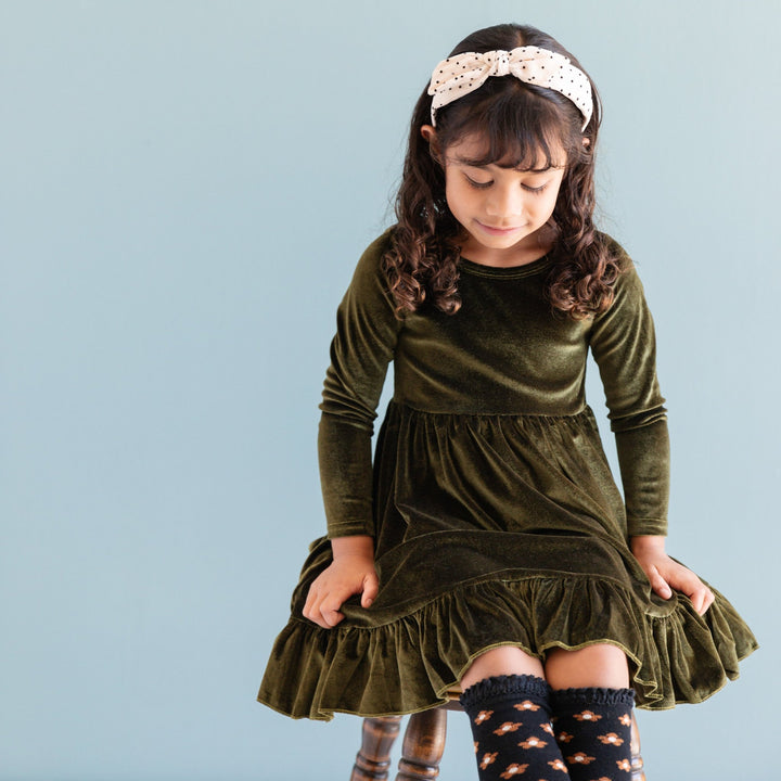 little girl in fall velvet long sleeve charm dress in green with black floral knee highs and cream headband with sheet black dot overlay