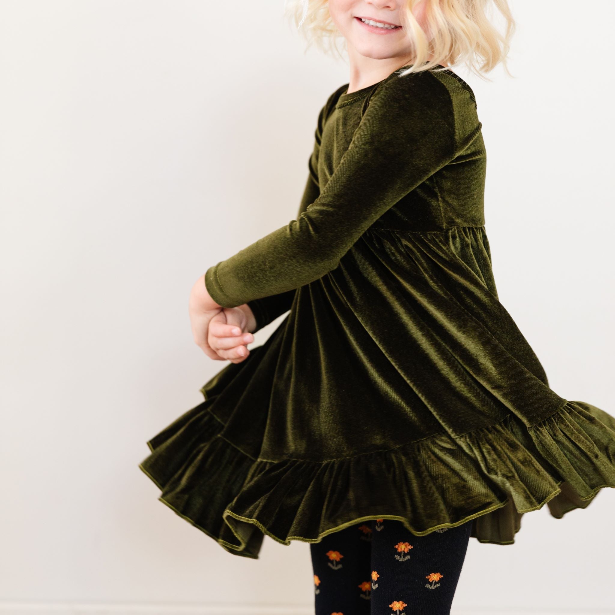 little girl twirling in long sleeve harvest green velvet twirl dress and matching floral knit tights