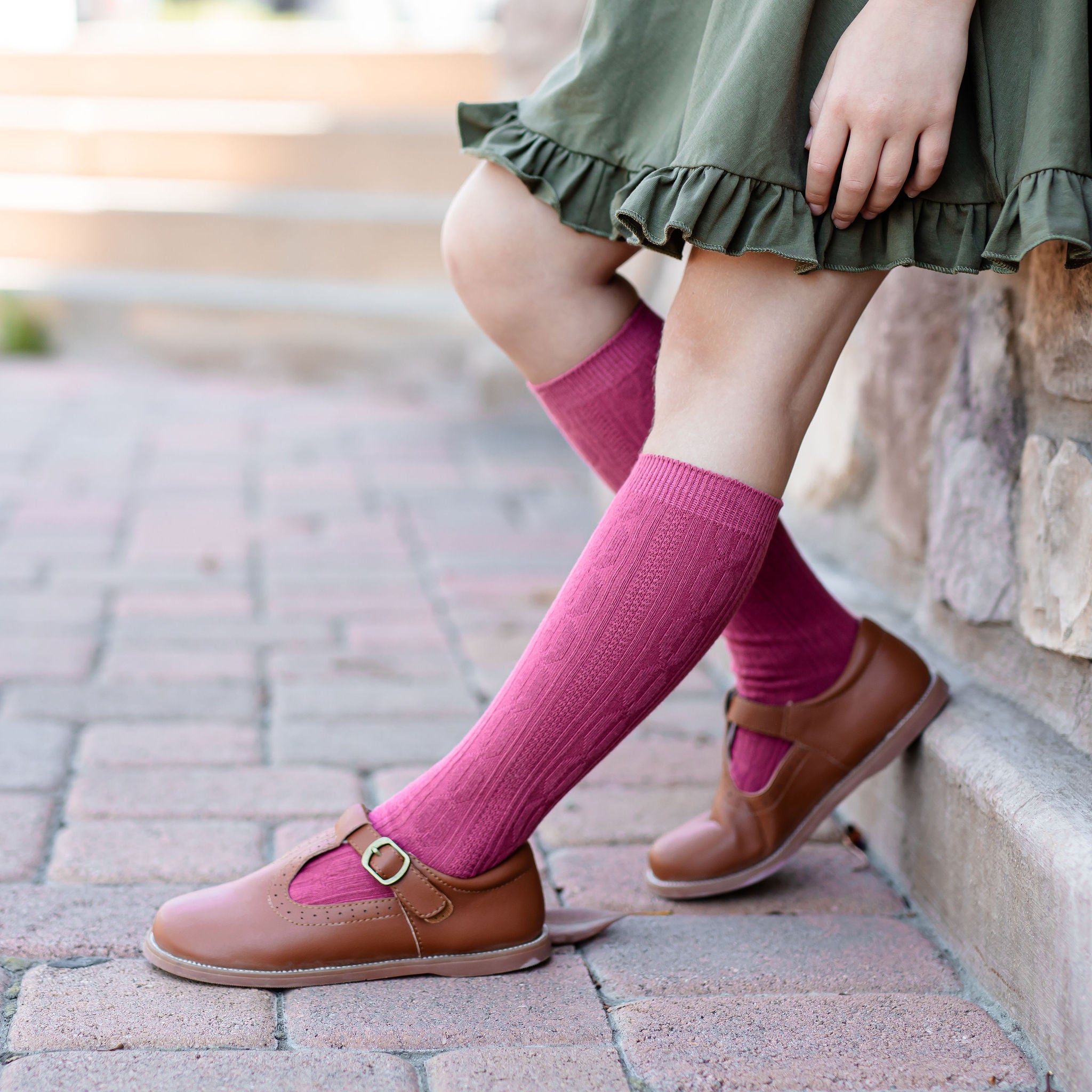 little girl wearing olive green ruffle hemmed dress with cute mulberry pink cable knit knee high socks and brown leather shoes