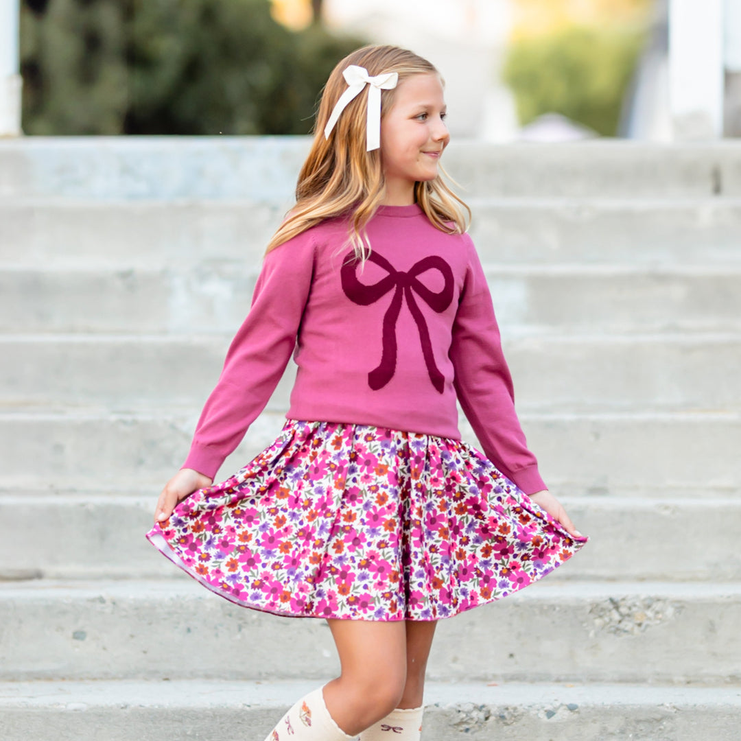little girl with mulberry knit sweater with burgundy bow design and matching fall floral skort