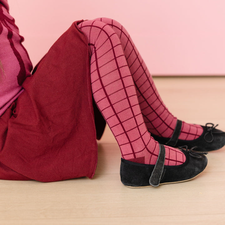 little girl sitting in mulberry tights with burgundy grid pattern and matching burgundy skort for fall