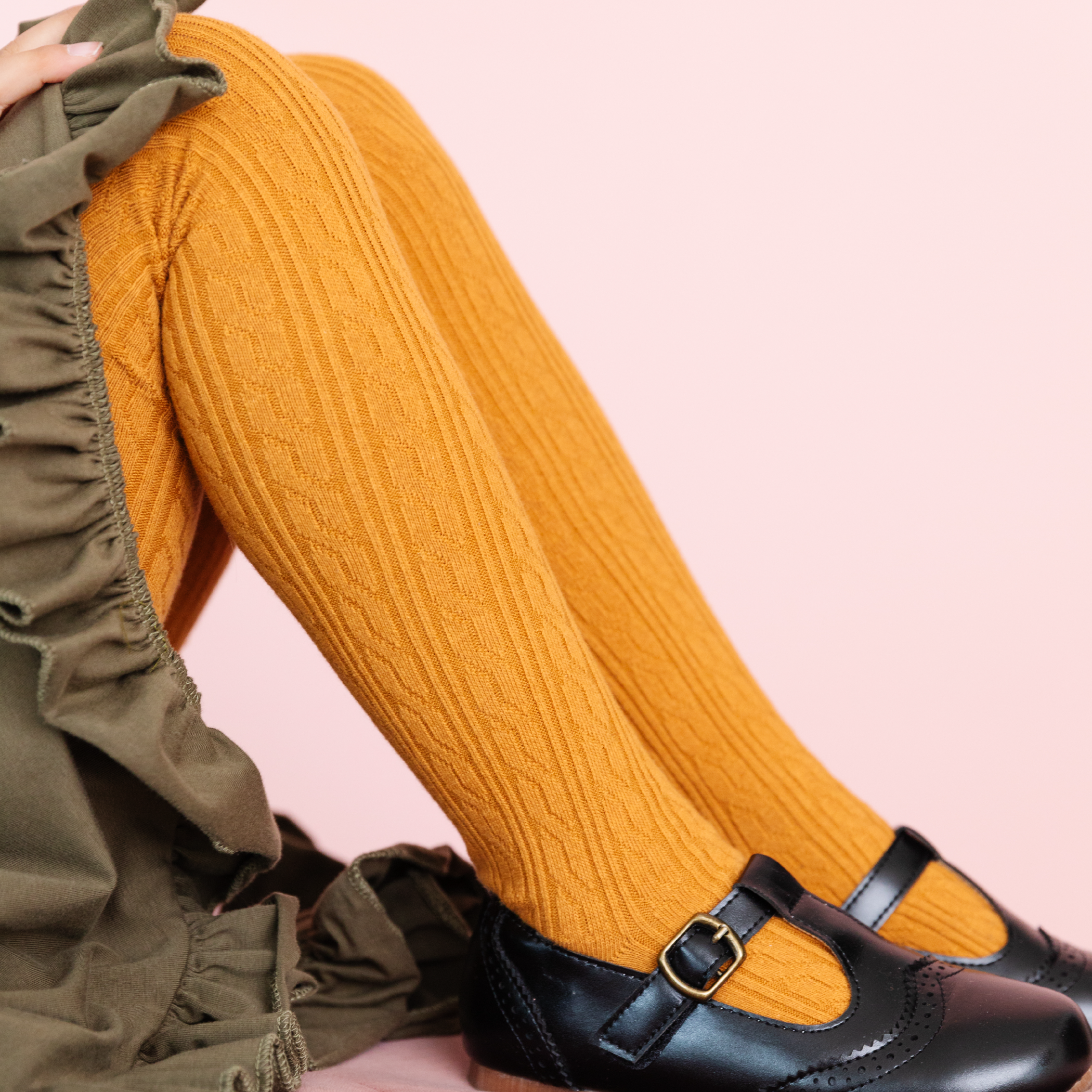 girl wearing mustard yellow cable knit tights and olive dress and black leather shoes