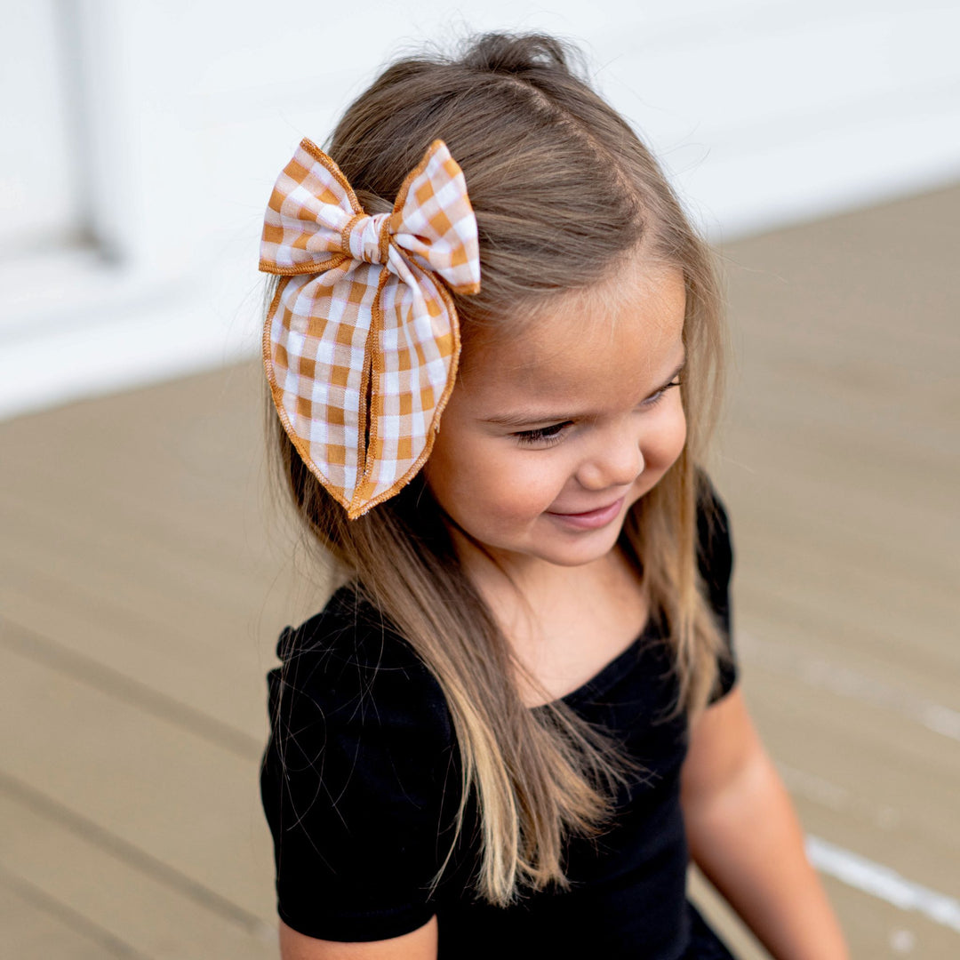 little girl in black dress wearing mustard gingham print hair bow