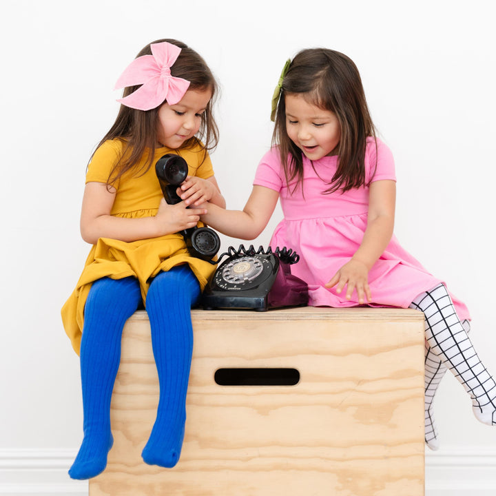 two girls playing with old phone in fall dresses and tights