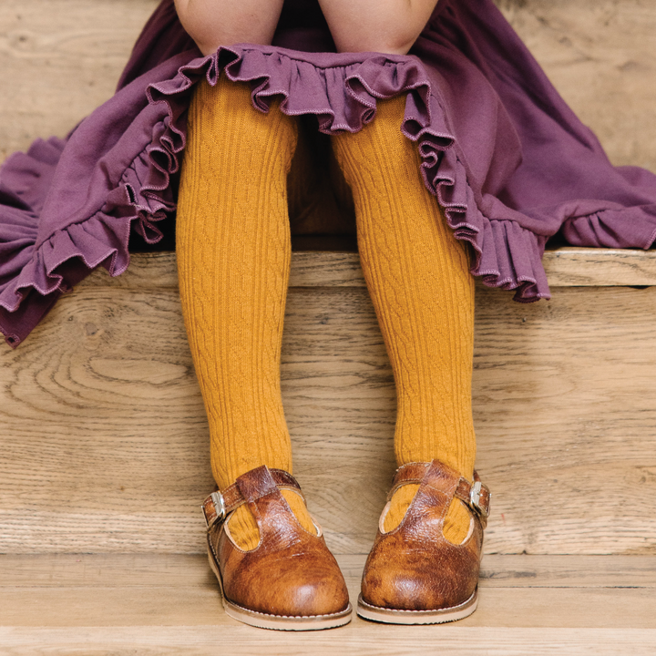 girl sitting on wooden stairs wearing mustard yellow cable knit tights and purple dress