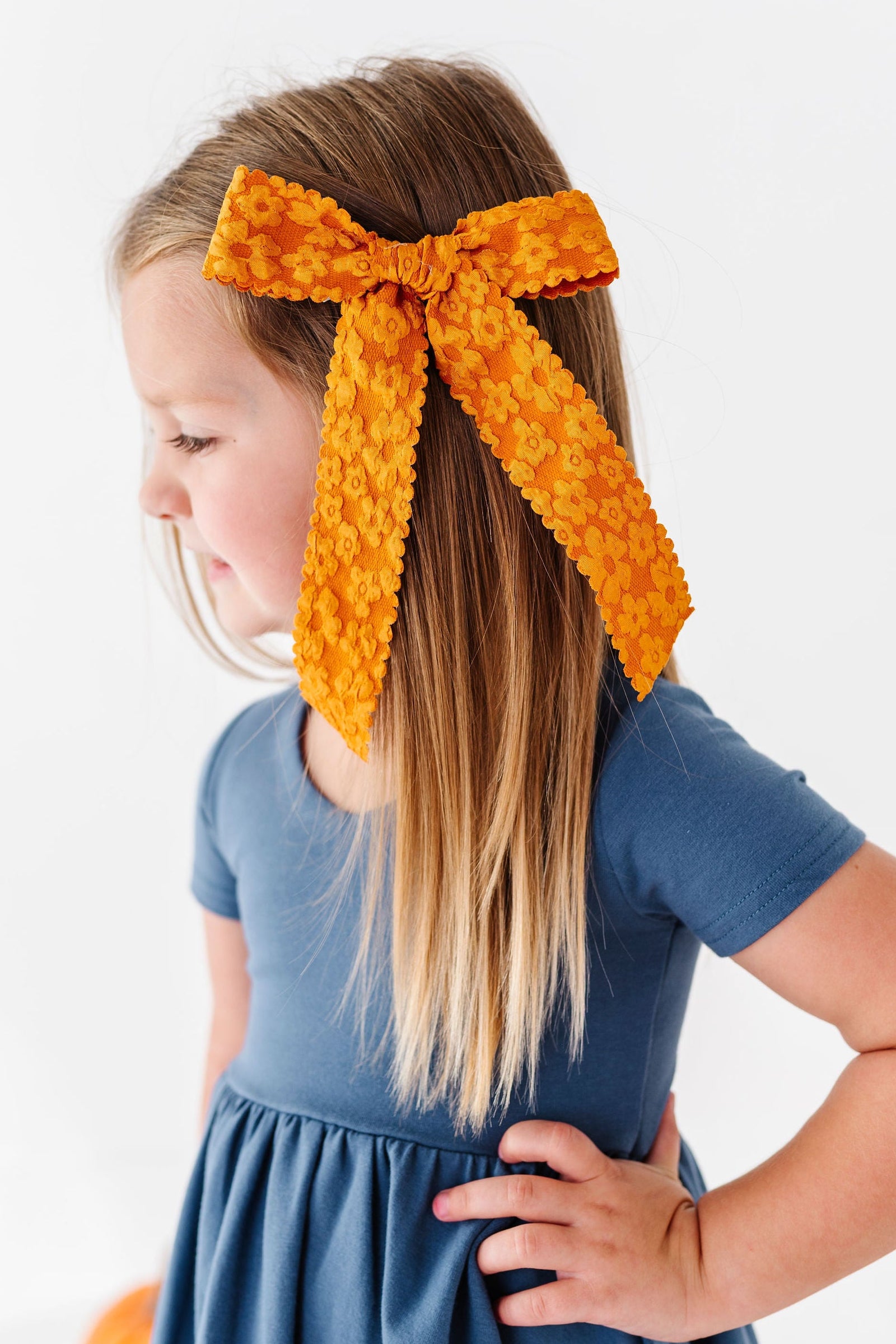 girl wearing mustard yellow hair bow with floral texture and blue dress