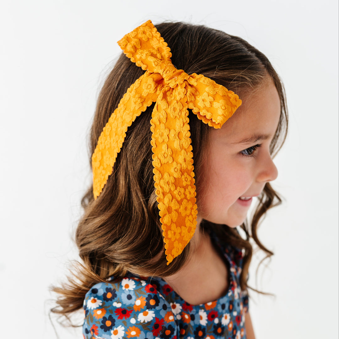 young girl in mustard bow with floral pattern and scalloped edges paired with blue fall floral twirl dress
