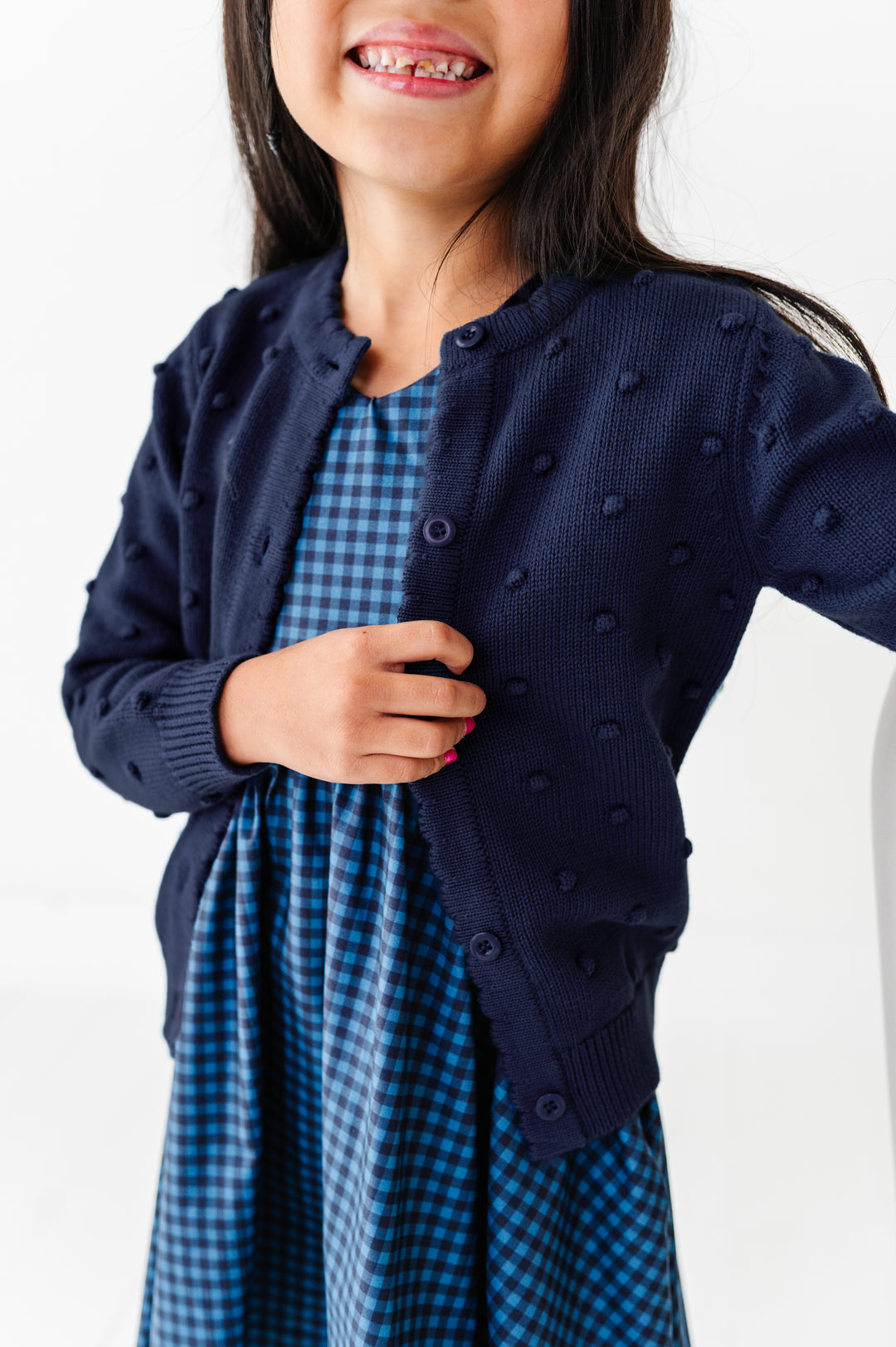 girl wearing bubble knit navy cardigan with matching blue and navy gingham v-neck dress