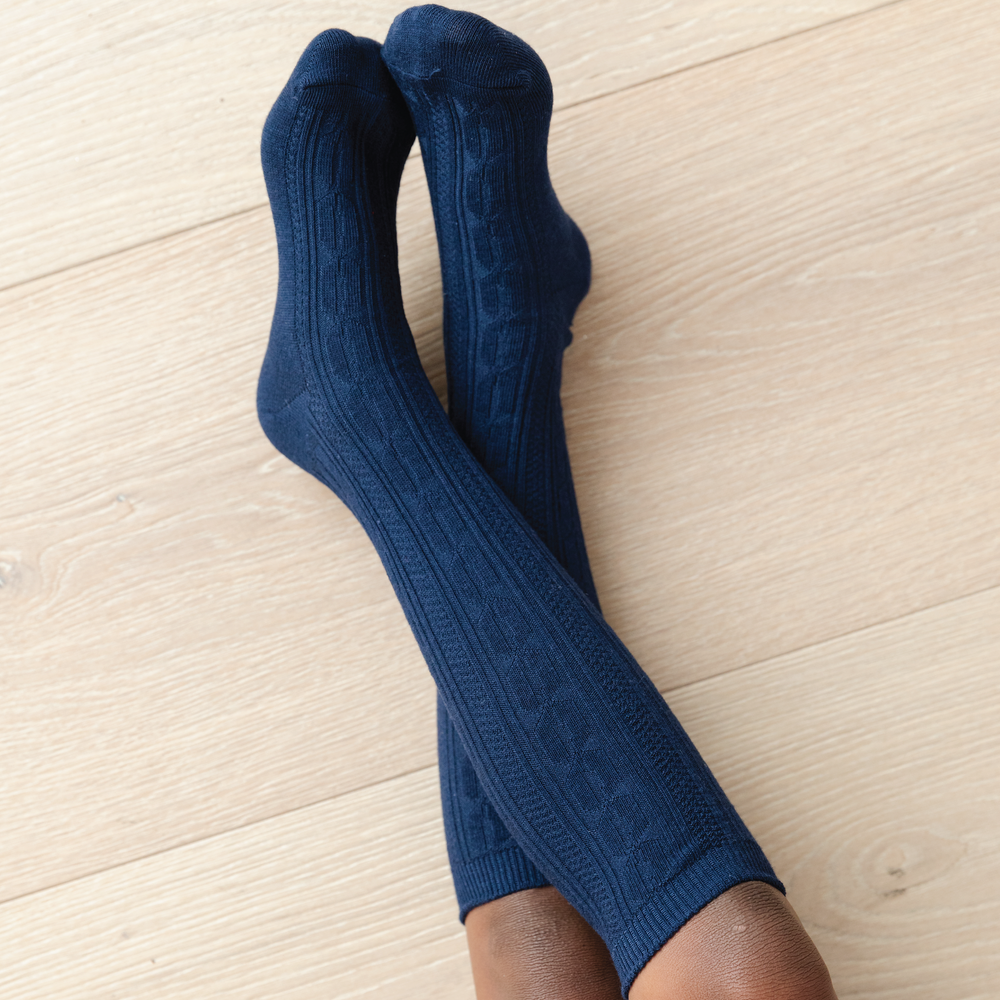 navy blue cable knit knee high socks on girl with legs crossed on wood floor