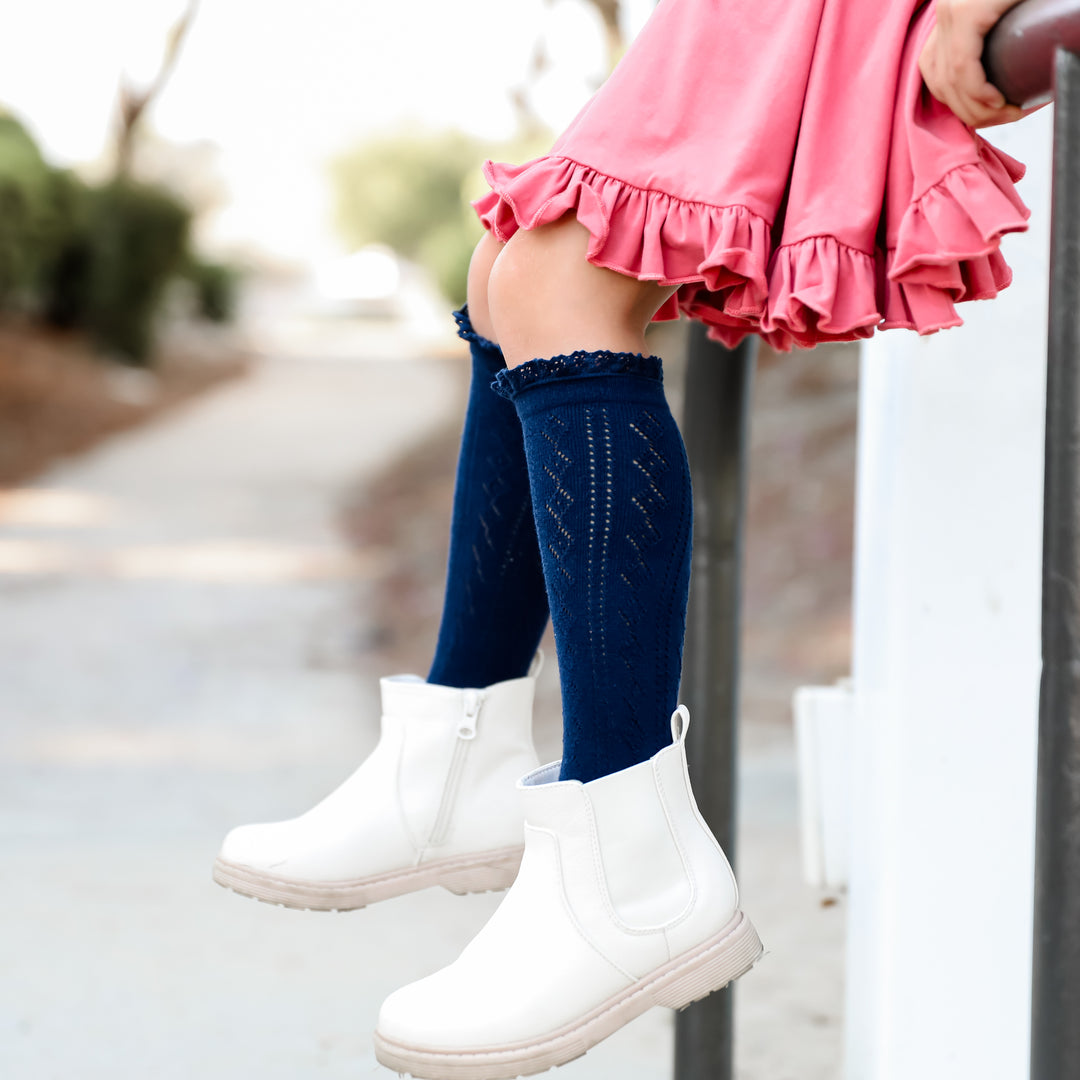 navy blue crochet knit knee high socks on little girl wearing pink twirl dress and white boots