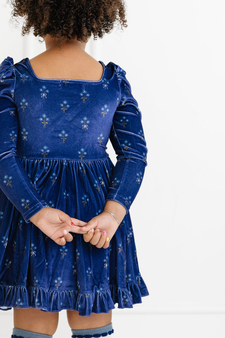 back view of little girl in square neck, long sleeve navy velvet twirly dress with petite flower bouquet pattern for fall