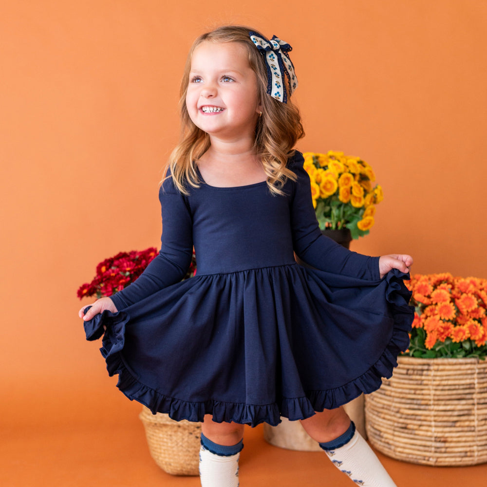little girl in front of fall flowers in navy long sleeve twirl dress paired with ivory and blue floral socks and bow