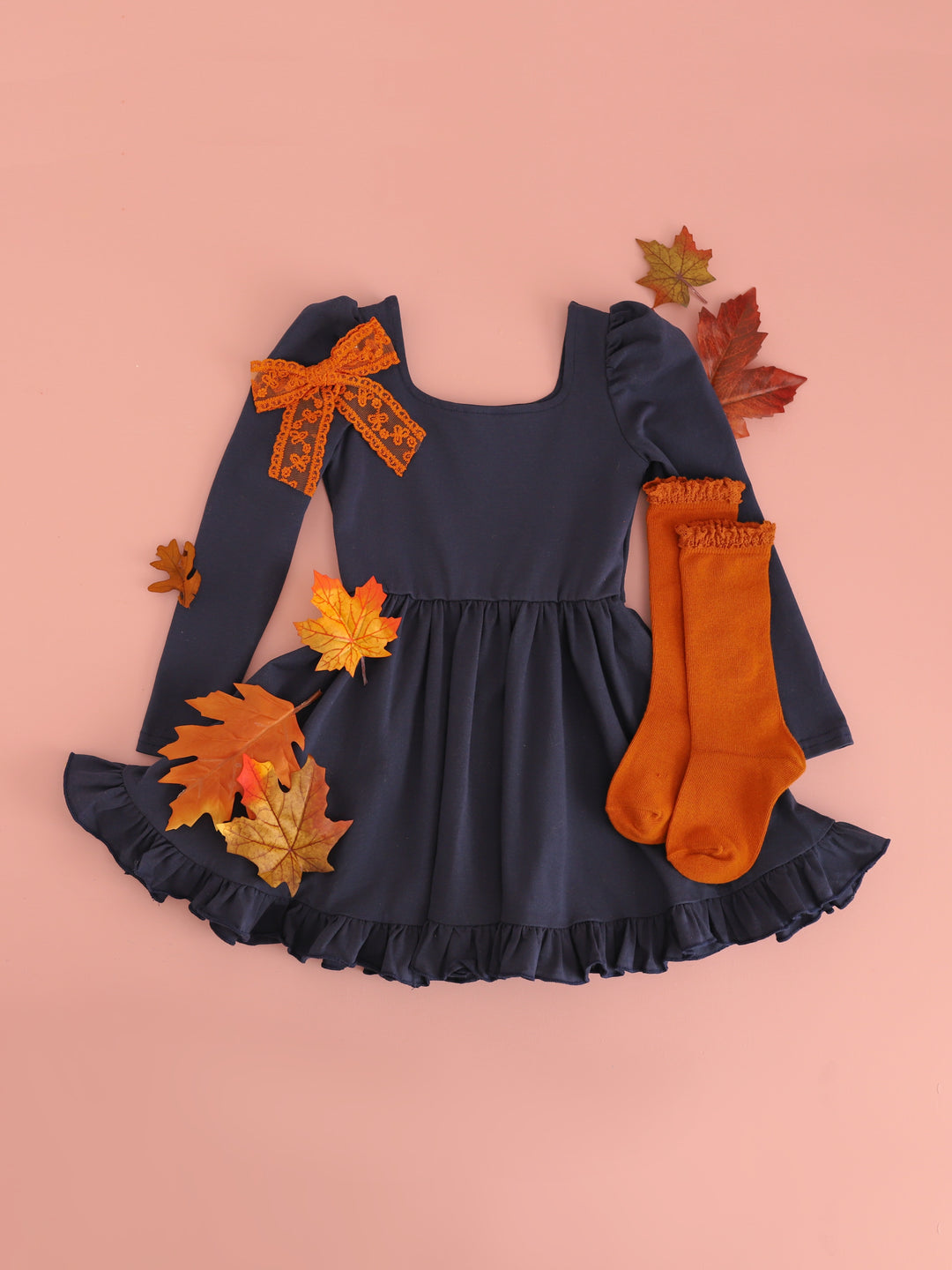 girls navy long sleeve twirl dress surrounded by fall leaves and paired with pumpkin spice orange knee socks and lace bow