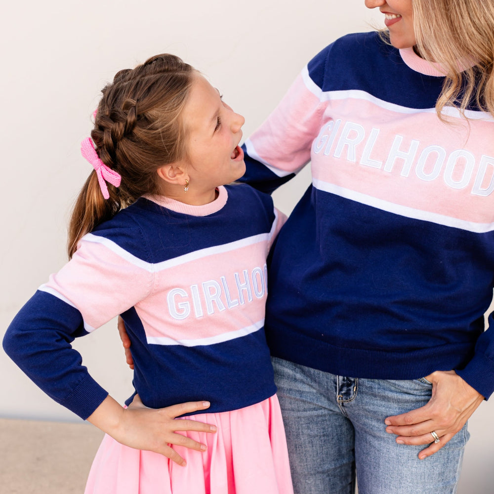 little girl and mother in matching navy and pink pullover knit sweater with girlhood embroidered patch across chest 
