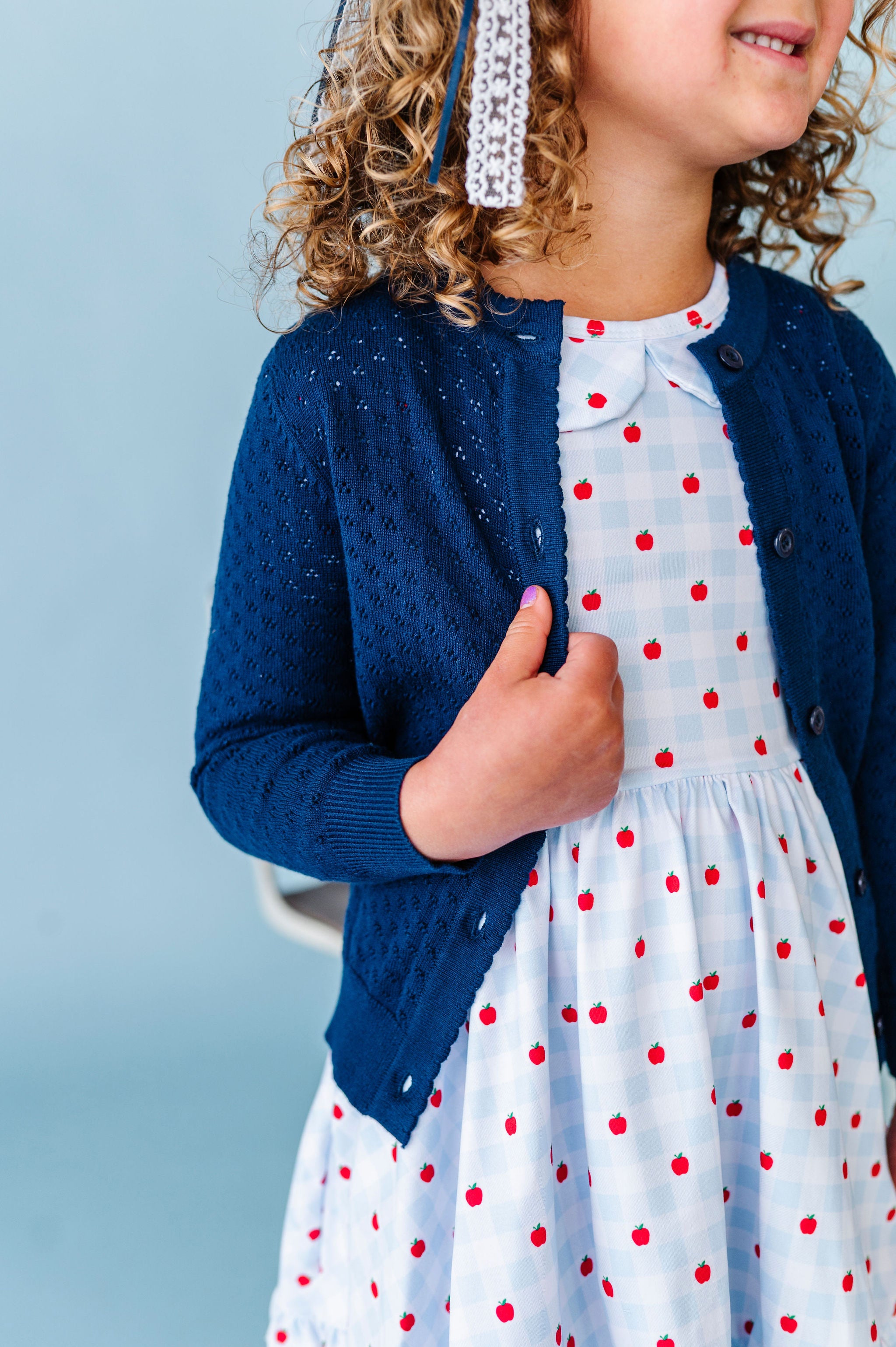 girl wearing navy pointelle knit cardigan over light blue and white apple dress for back to school