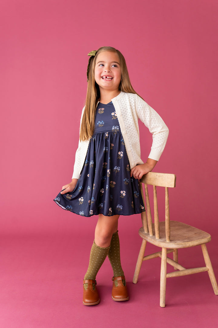 young girl in navy blue fall floral twirl dress paired with ivory pointelle cotton knit cardigan and olive bow and knee socks