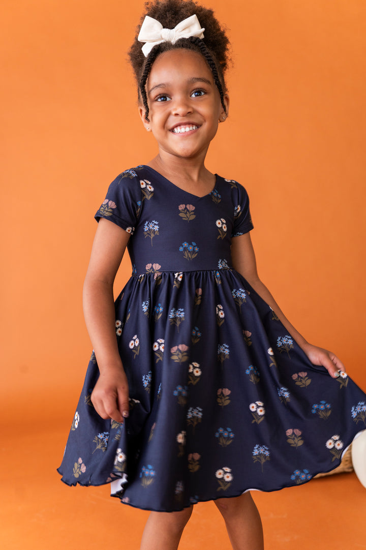 little girl posing in navy blue floral v-neck twirl dress paired with ivory velvet hair bow