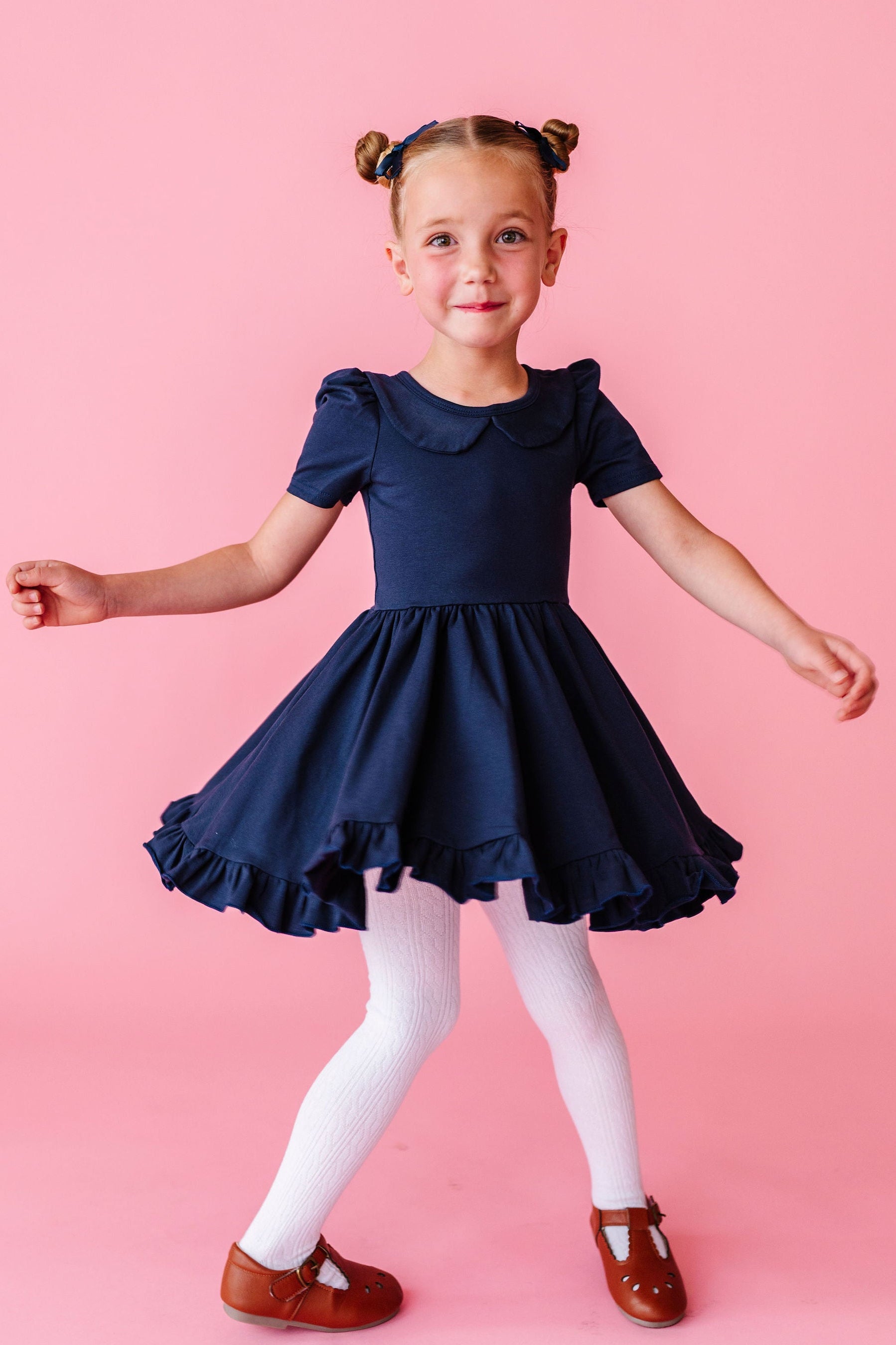 girl twirling in navy cotton dress with collar and white cable knit tights