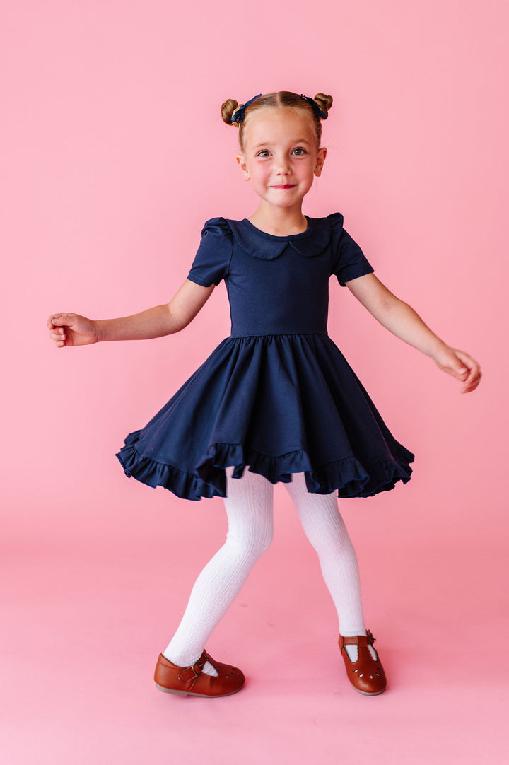 girl twirling in navy cotton dress with collar and white cable knit tights