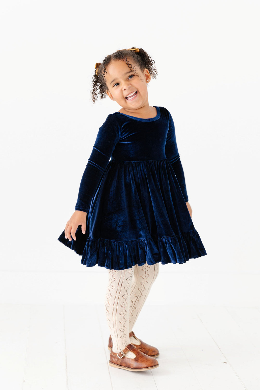 little girl in navy blue long sleeve velvet holiday dress with cream open knit tights and gold pigtail bows